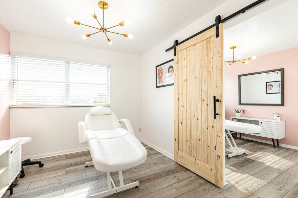 Space with a comfortable white chair in the examination room. The walls are white with natural elements, such as wood floors and wooden barn-type door.