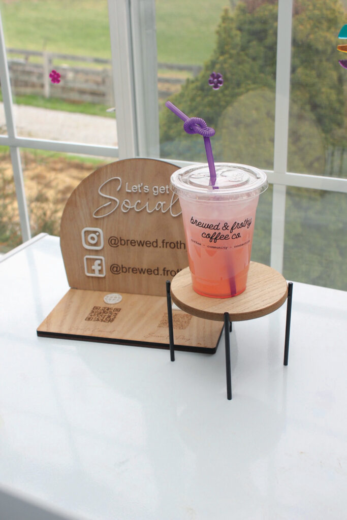 A plastic cup of iced fruit tea sits on a table with a wooden circular sign for Brewed & Frothy Coffe Co.